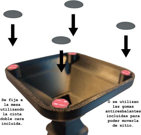 Un primer plano del Soporte para Auriculares y Cascos Universal en Mesa, que presenta un diseño trapezoidal negro con almohadillas circulares rojas en cada esquina. Las flechas negras apuntan a las almohadillas mientras el texto en español explica los métodos de montaje: usando cinta de doble cara o almohadillas de goma antideslizantes.