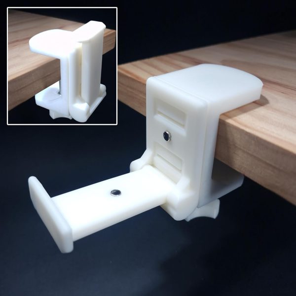 Primer plano del "Soporte Auriculares para Mesa, Seguro y Resistente", una abrazadera de plástico blanco sujeta firmemente al borde de una superficie de madera. Este soporte plegable para auriculares cuenta con un mecanismo deslizante ajustable con un tornillo para apretar y viene con almohadillas protectoras de goma para evitar daños a su escritorio. Un recuadro muestra un ángulo diferente de la abrazadera, destacando su diseño y método de fijación. La pinza soporta hasta 3kg.